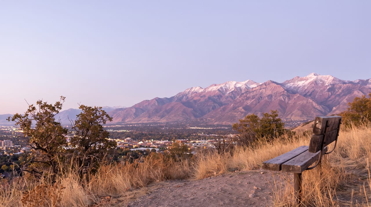 The Wasatch Range at dusk over Salt Lake City, fresh snow on the peaks lit rose and violet, the downtown skyline small in the middle distance